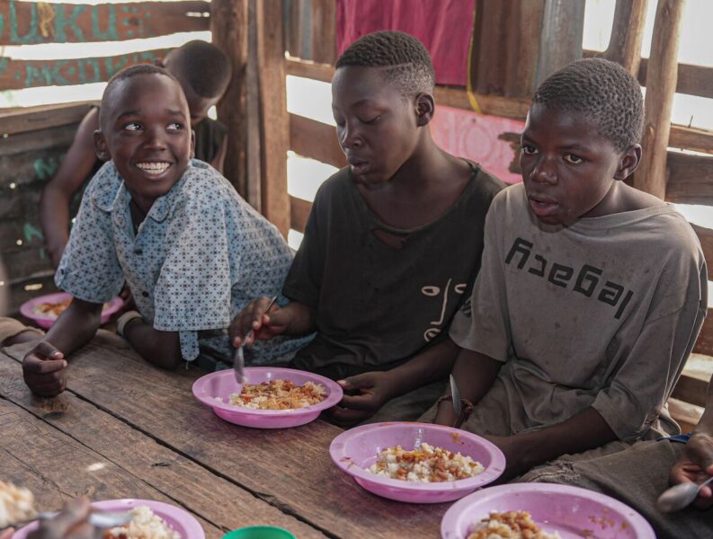 Three boys sat at a table eating food together.