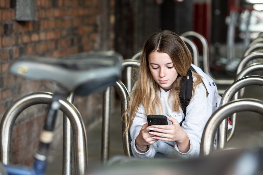 A teenage girl sat outside a train station looking down at her phone and texting.