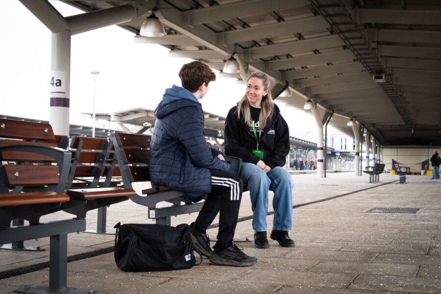 Railway Children worker speaking to child on bench on train platform