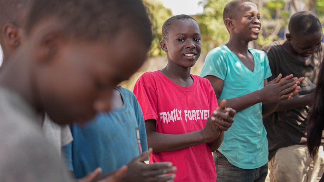 A group of teenage boys on the streets of Tanzania clapping their hands and smiling.