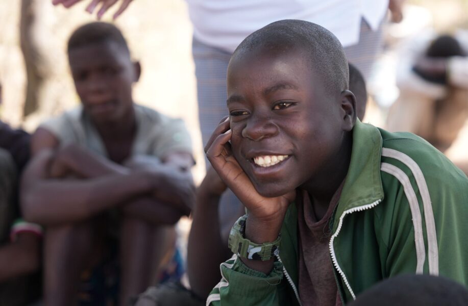 Boy with his head in his hand smiling, wearing a green jacket.