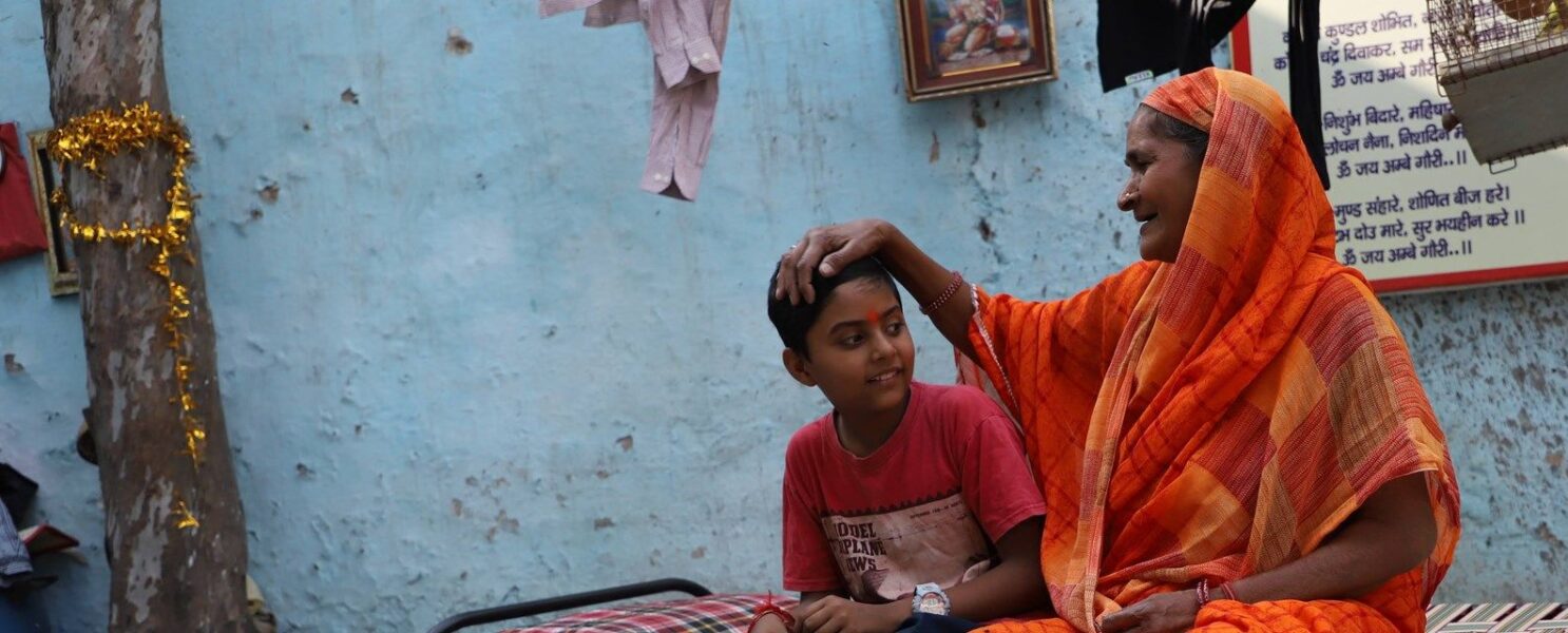 A grandmother sitting with her grandson and smiling, with her hand placed on his head.